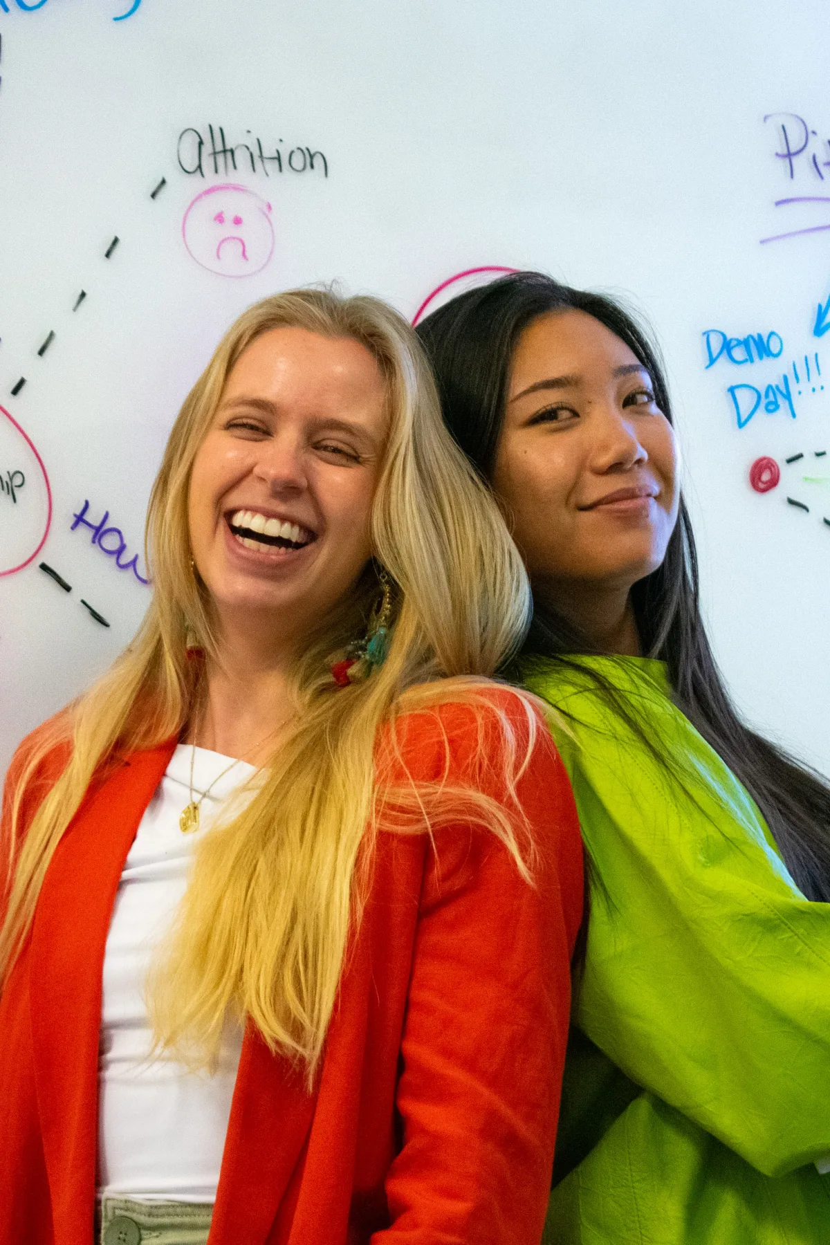 Two students laughing in front of a whiteboard covered in ideas.